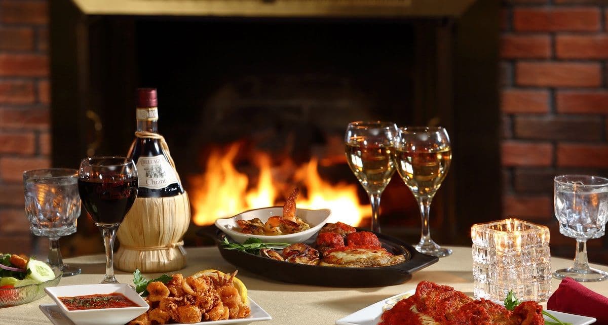 A candlelit table by the brick fireplace set with red and white wine and a bottle of Chianti